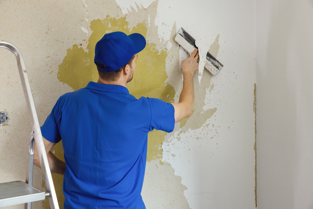 Worker removing old painted wallpaper from a wall in a Union City business