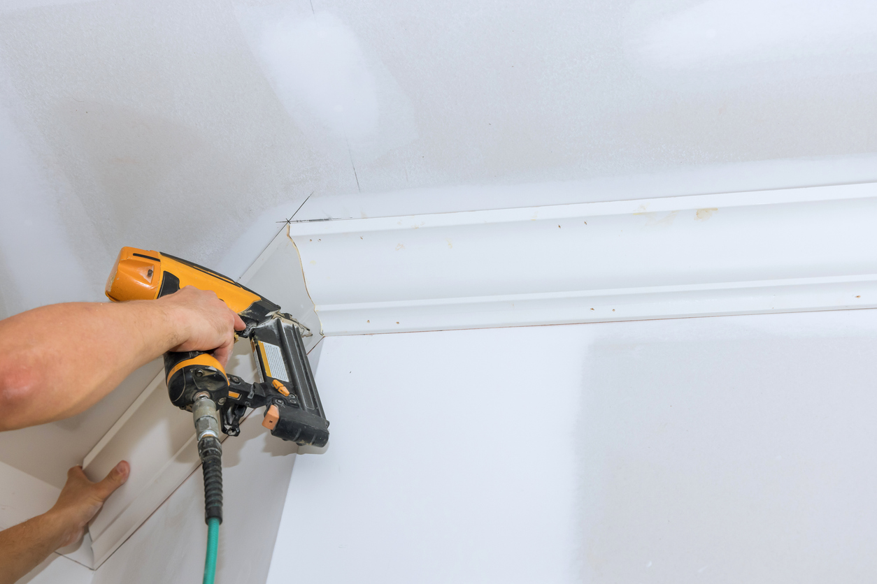 Using an air nail gun a carpenter installs the crown molding on the corners of the ceiling in a Newark CA home