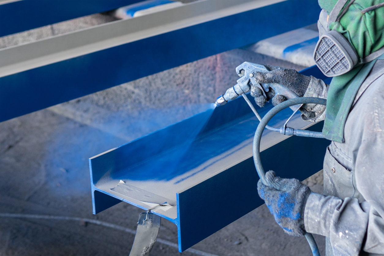 Painting color top coat on steel structure with spray gun at industrial factory in San Jose.