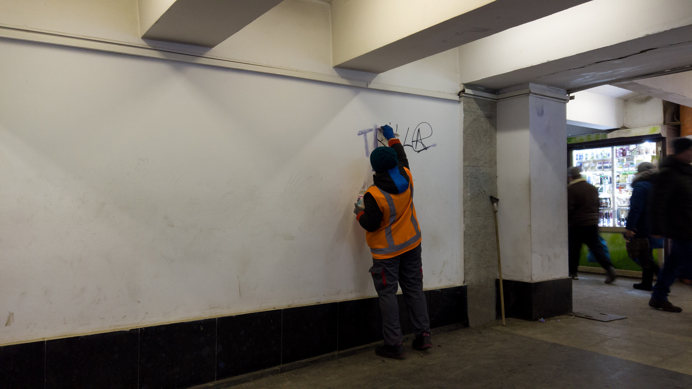 Removing graffiti and paint from vandals. an employee of the city, wearing a orange uniform, cleans the wall from graffiti and writing, with a liquid solvent in a Santa Clara area business